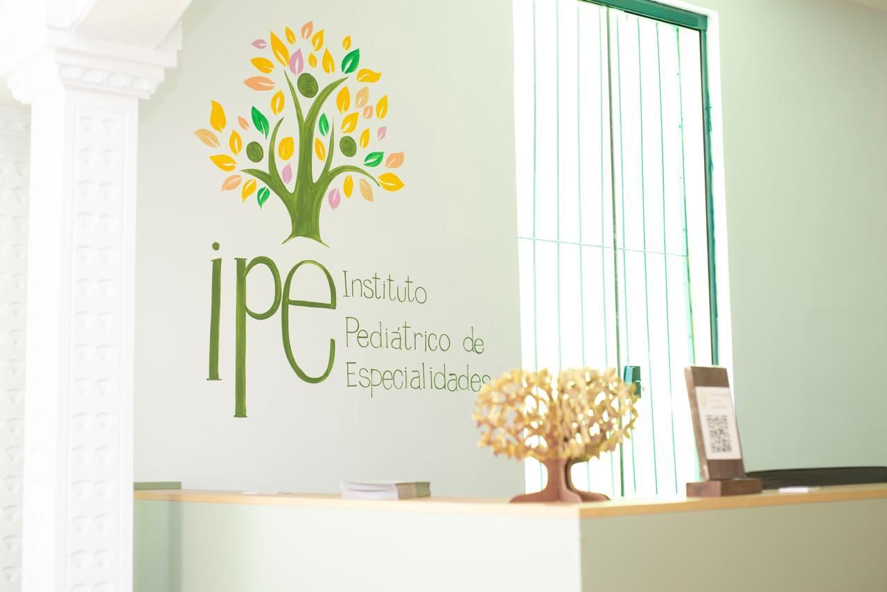 Recepção da Clínica IPÊ, com a árvore-símbolo do Instituto Pediátrico de Especialidades pintada na parede acima do balcão de atendimento